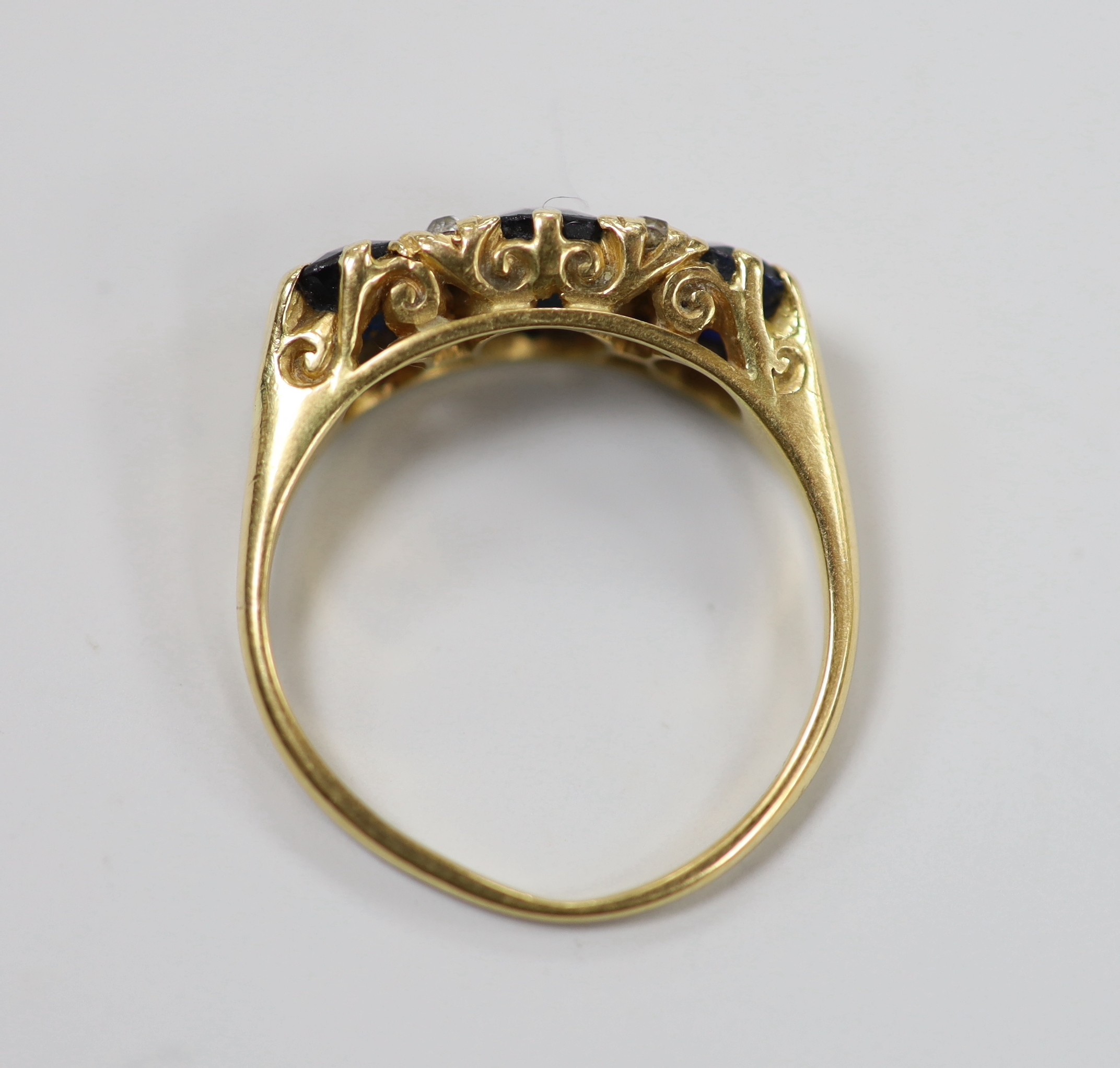 An early to mid 20th century gold, three stone sapphire and four stone diamond chip set half hoop ring, size O, gross weight 4.5 grams.